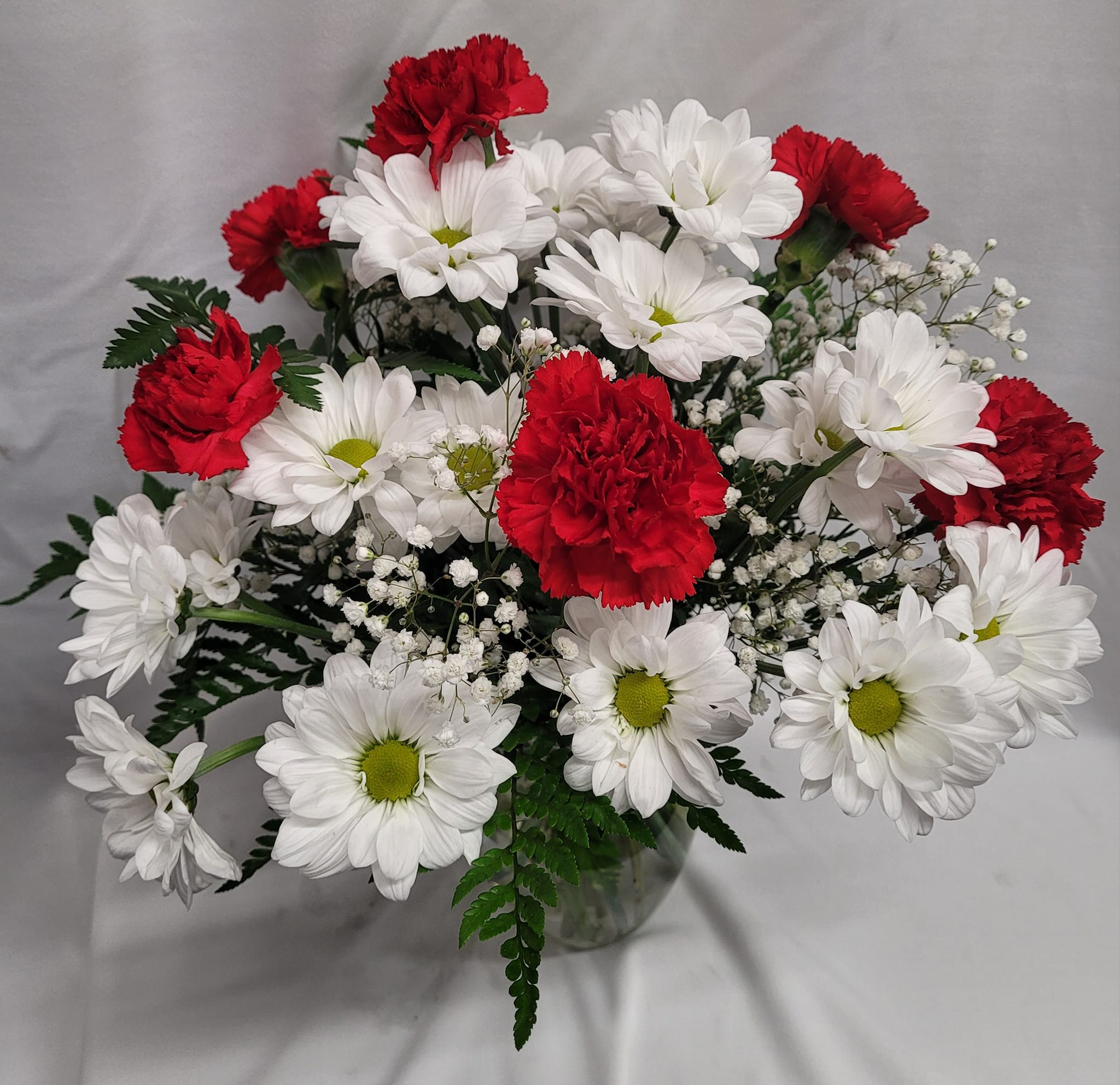 Bouquet of red carnations and white daisies in a clear glass vase