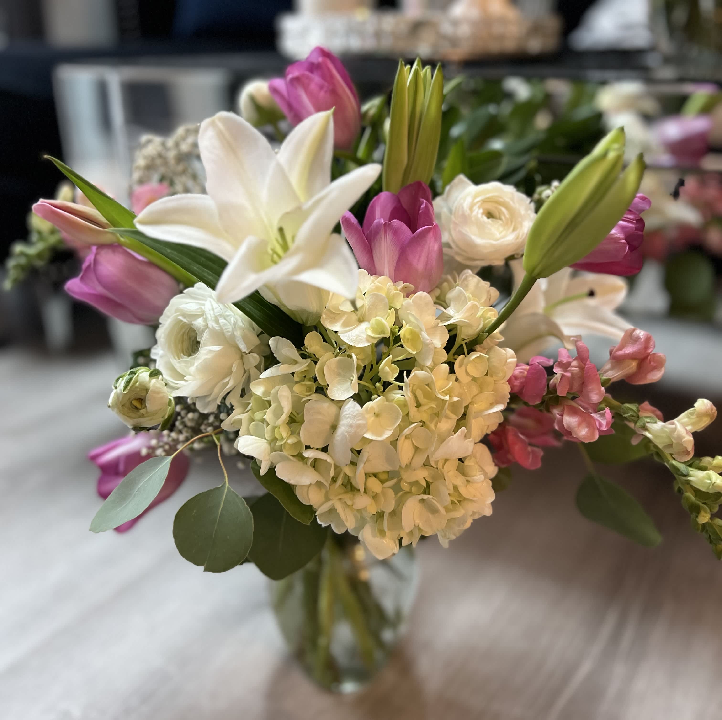 Mixed bouquet of white lilies, hydrangeas, and pink tulips in a clear glass vase