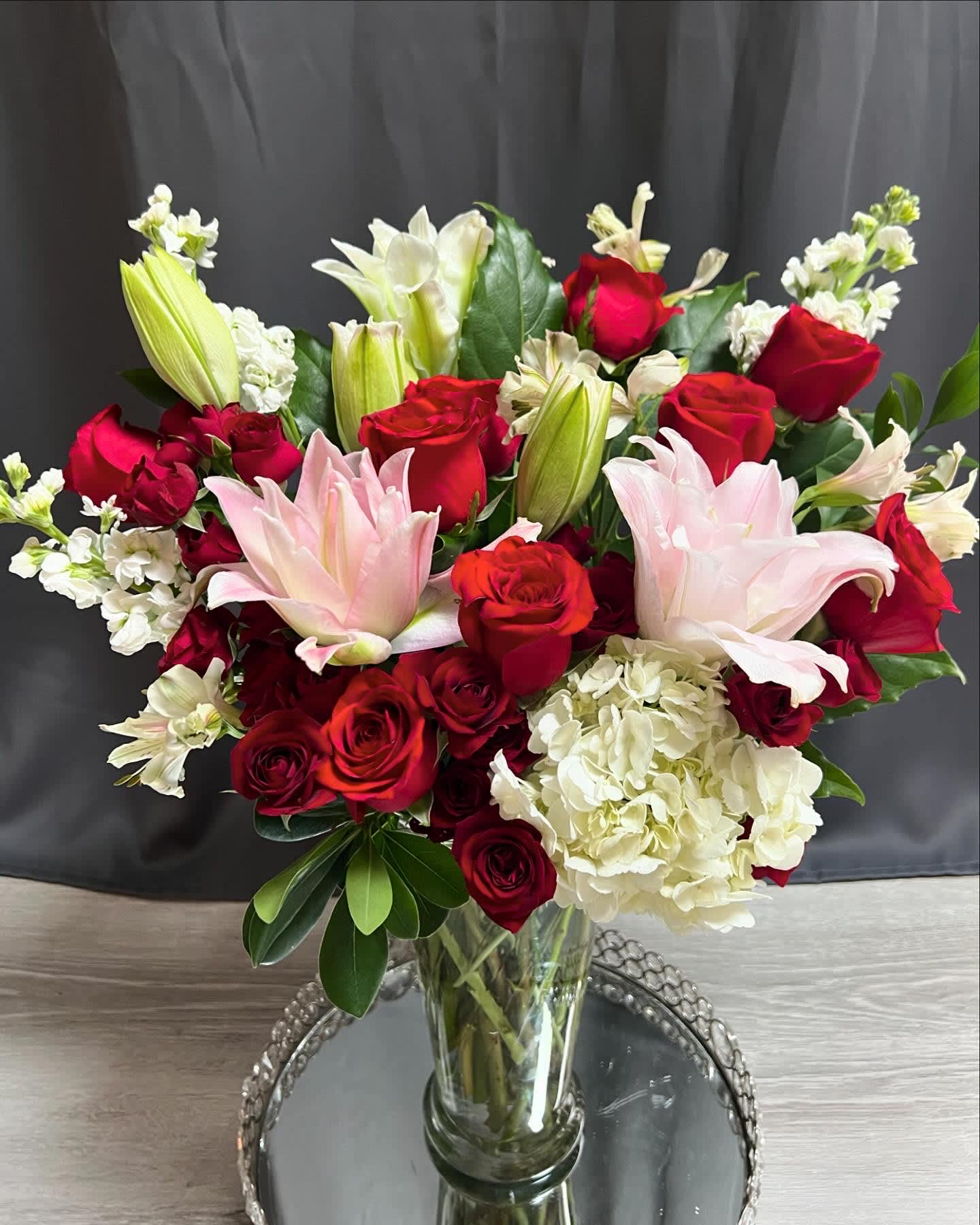 Bouquet of red roses, pink lilies, and white hydrangeas in a glass vase