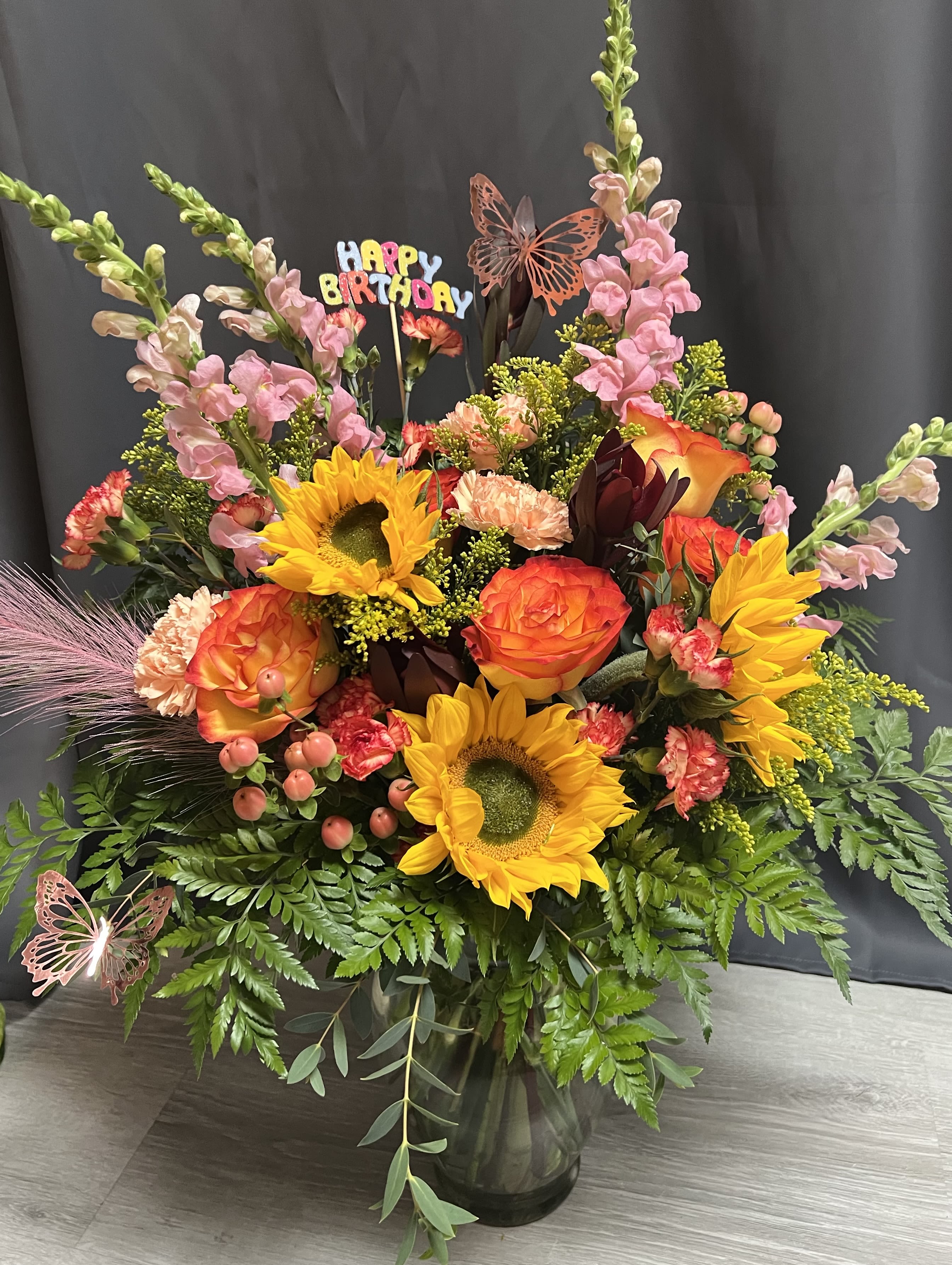 Colorful bouquet with sunflowers, roses, and pink snapdragons in a glass vase