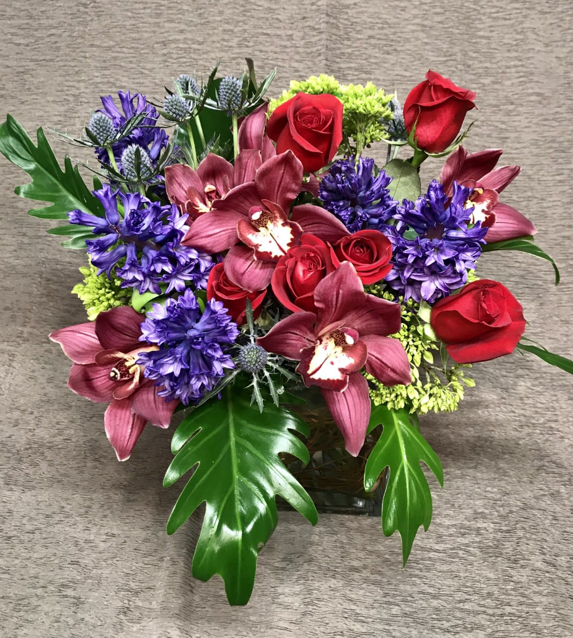 Orchid Rose Cube Deep Colors - Modern design of Cymbidium orchids, roses and jewel tone colors. Assortment and colors will vary.  Orchids may vary.  Please allow a minimum few days' notice for us to acquire fresh orchids.  Passionate colors. Nice choice for Valentine's day and anniversaries.