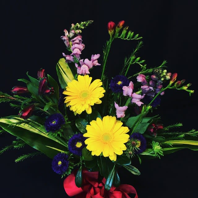 Bouquet of yellow daisies, purple blooms, and pink flowers with a red ribbon