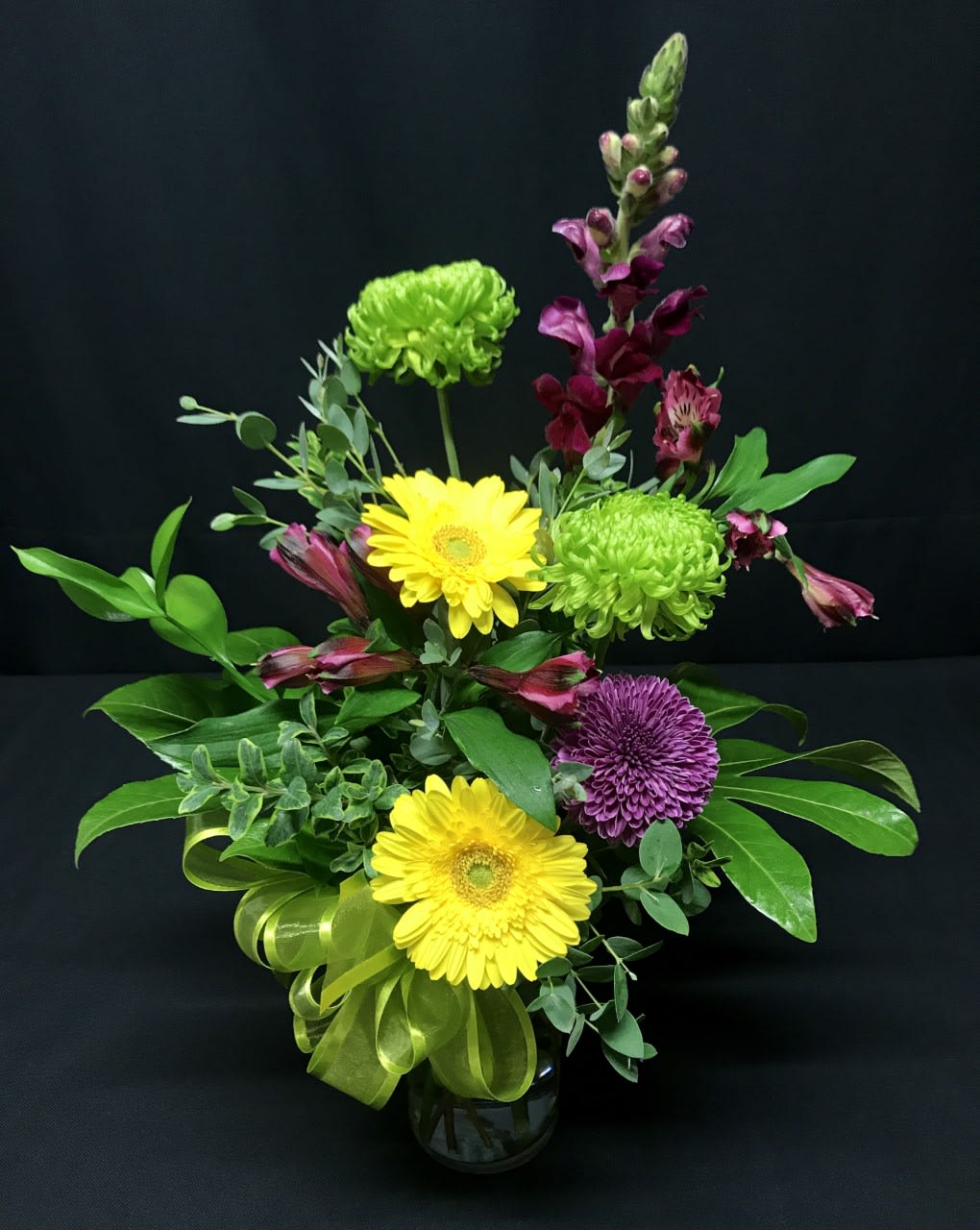 Mixed bouquet with yellow gerbera daisies, green chrysanthemums, and purple blooms in a vase