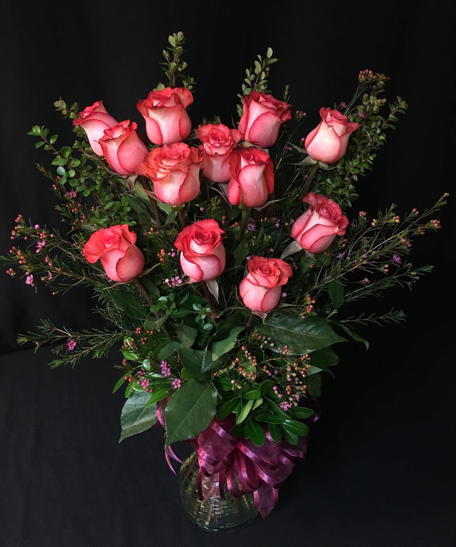 Pink roses arranged in a clear glass vase with a purple ribbon