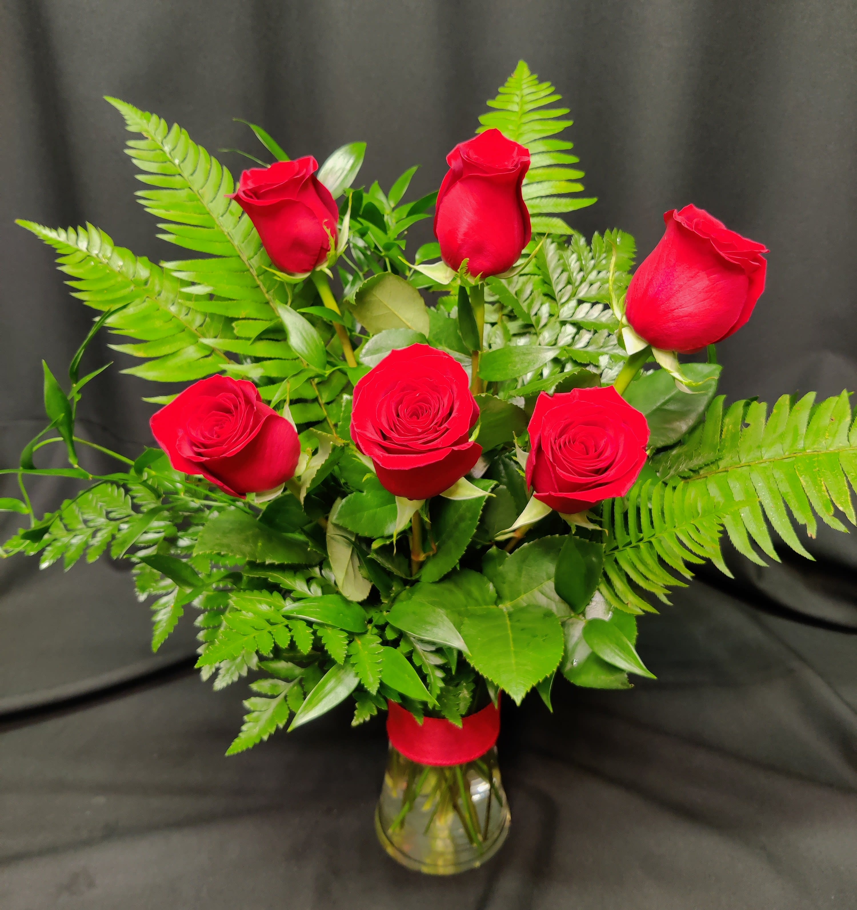 Bouquet of red roses with fern foliage in a clear glass vase