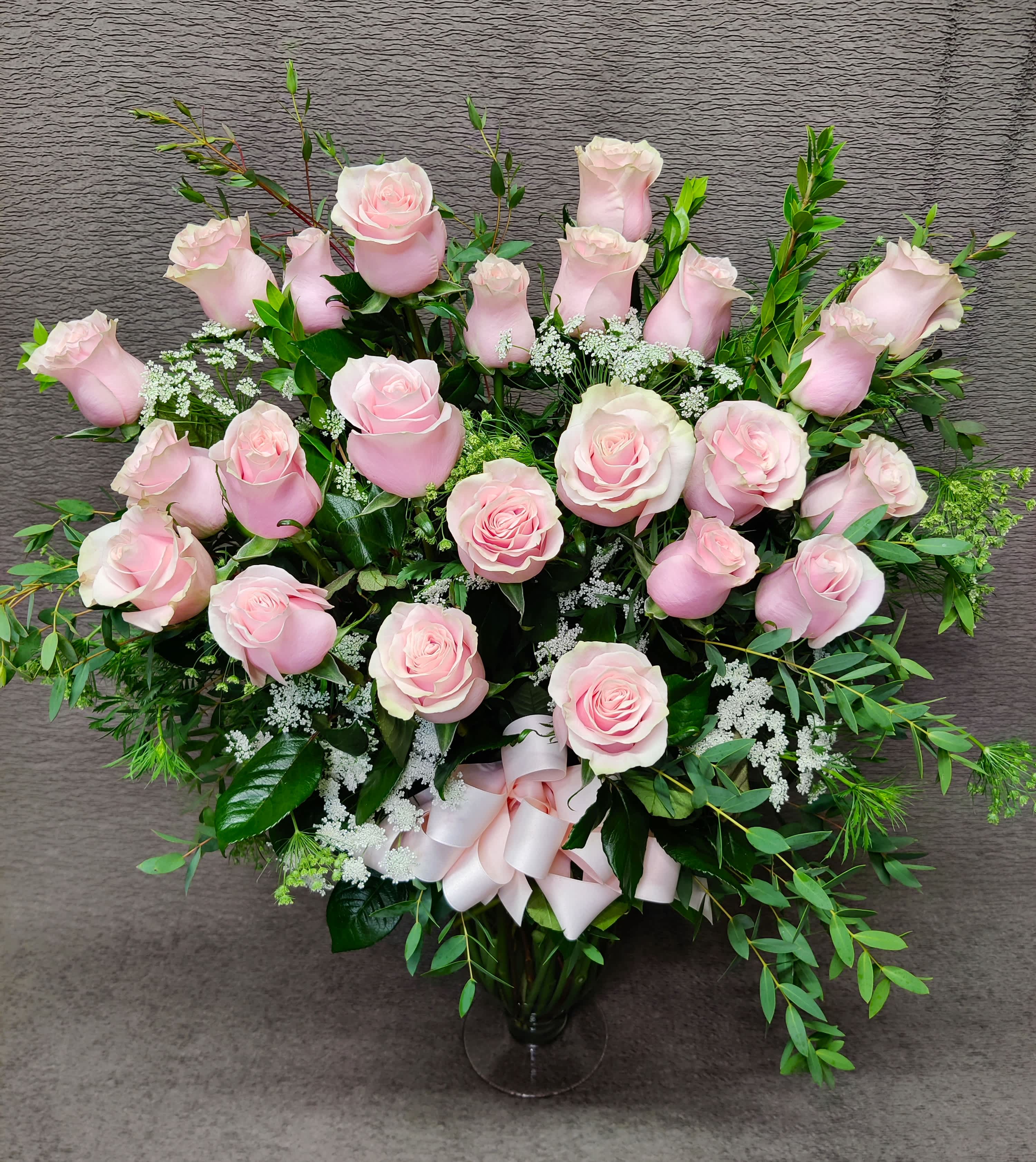 Pink roses arranged in a clear glass vase with a ribbon bow