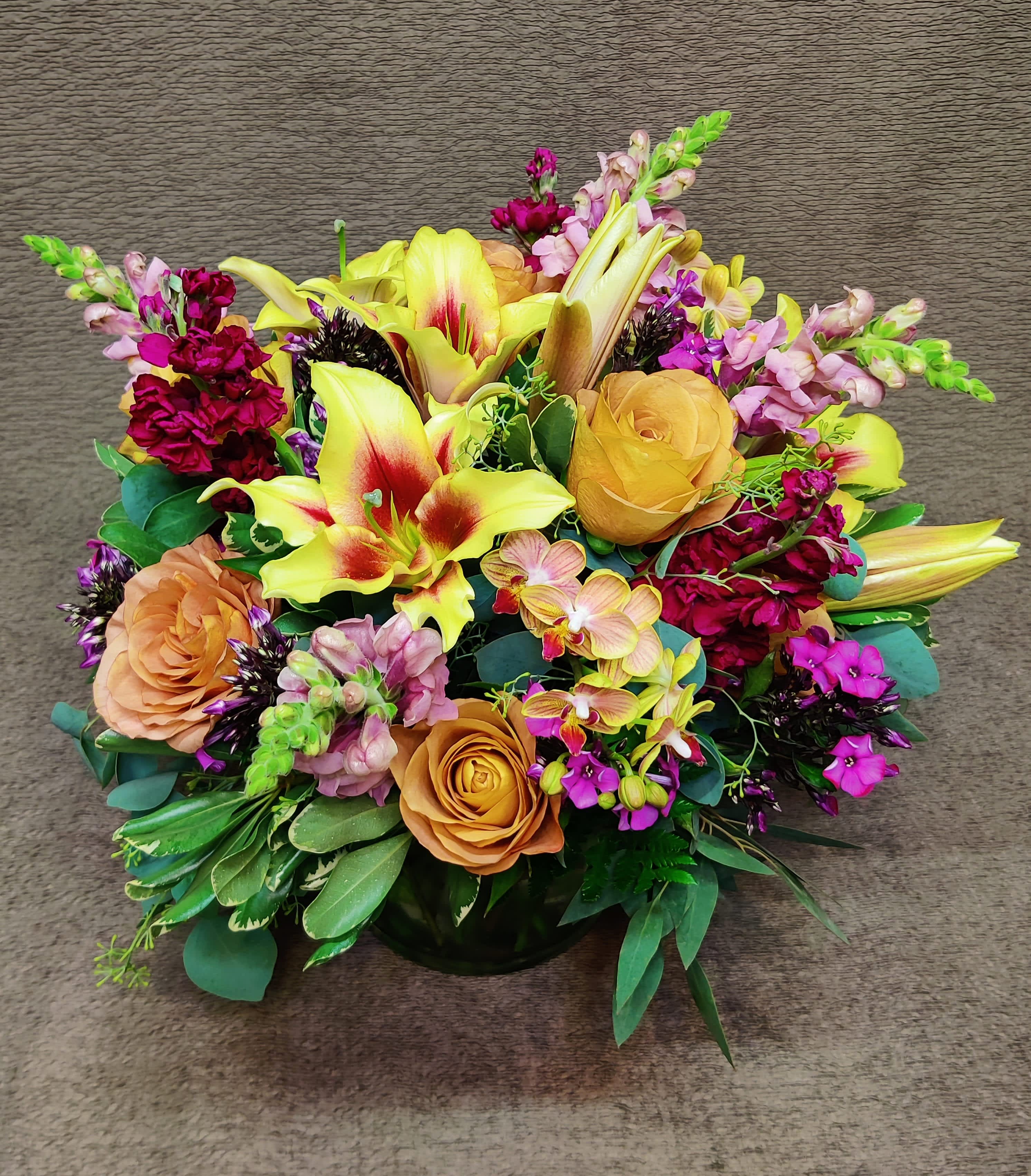 Mixed bouquet with yellow lilies, peach roses, and pink flowers in a low vase