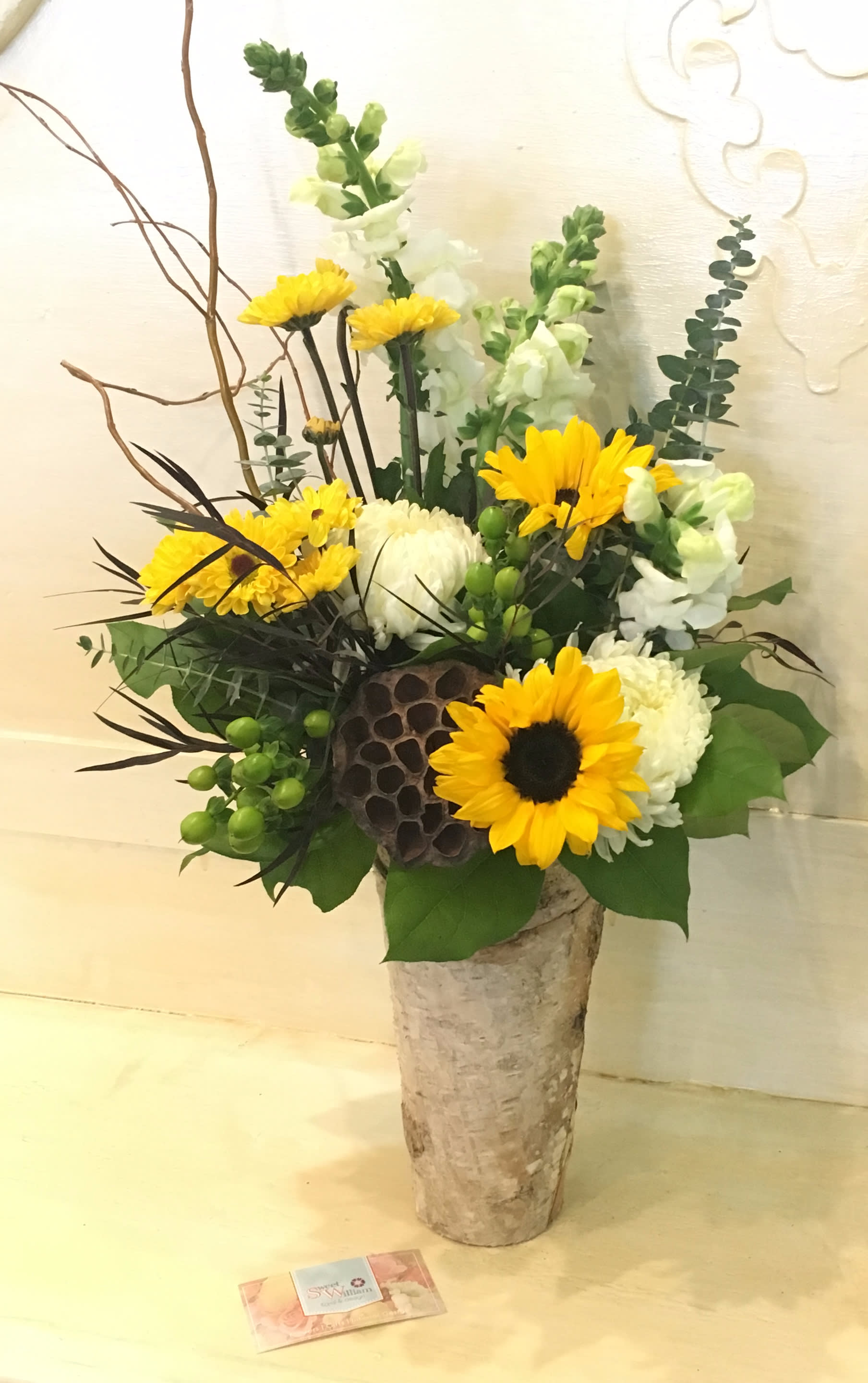 Tall floral arrangement with yellow sunflowers and white blooms in a birch-style vase