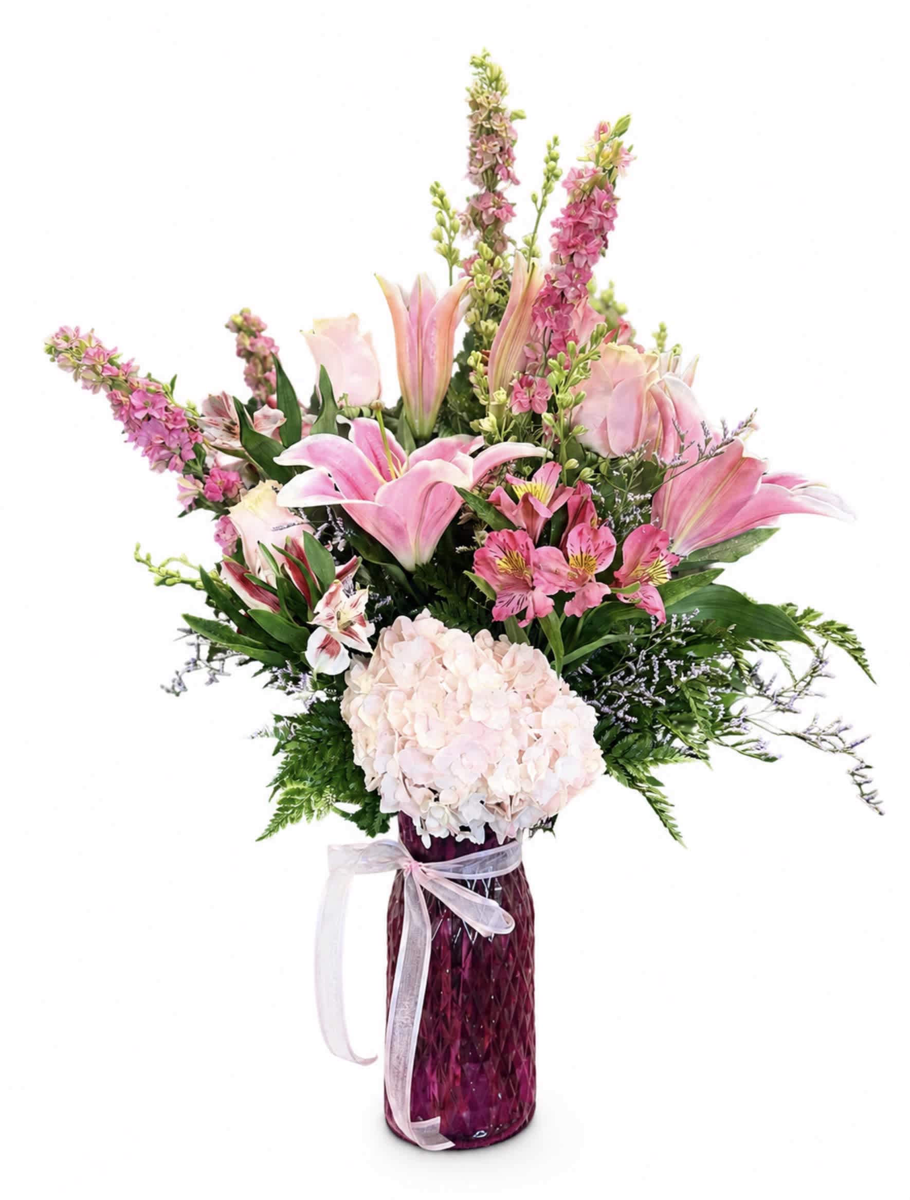 Pink lilies and hydrangea in a tall purple vase with a ribbon