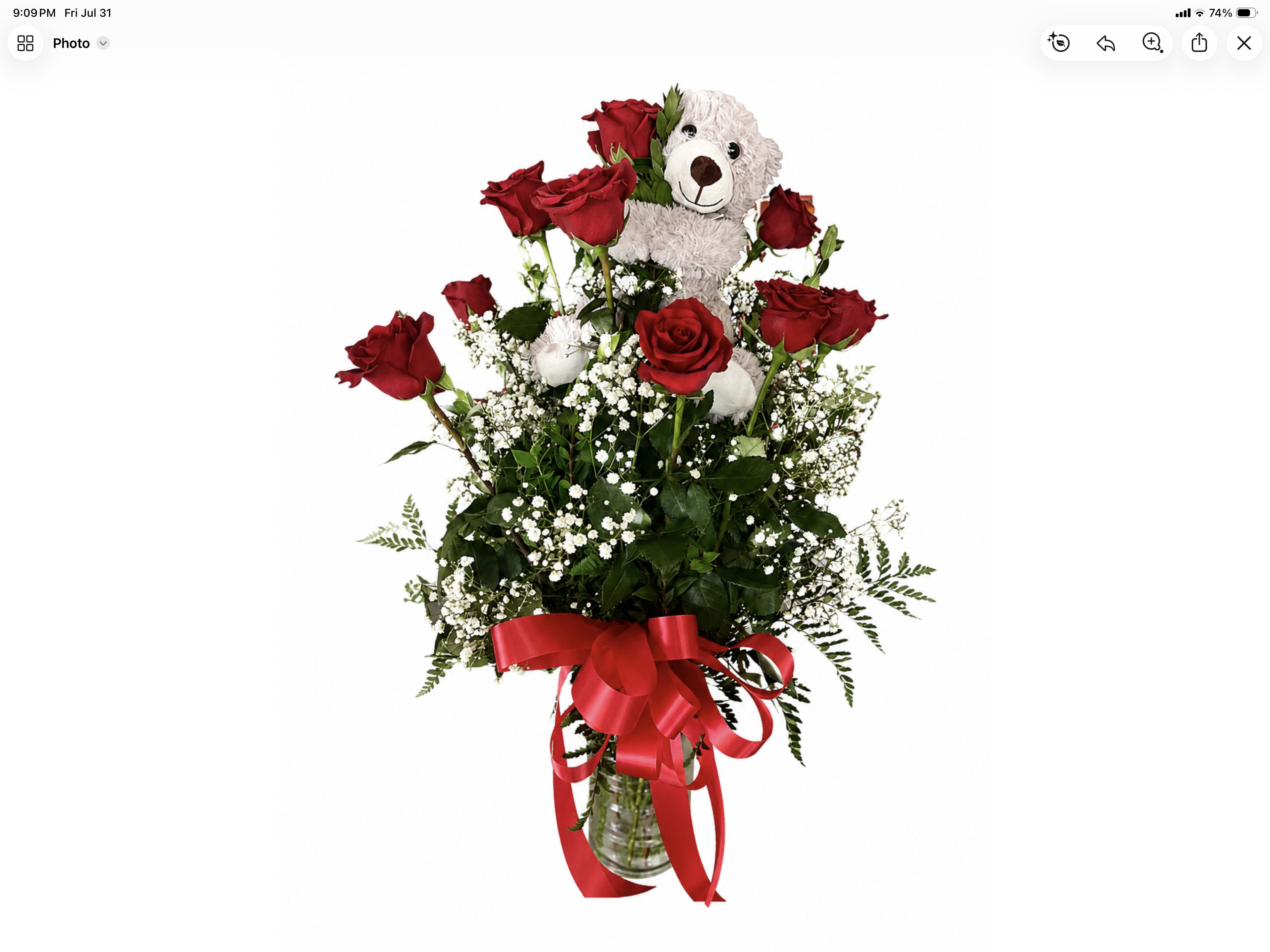 Red roses arranged with a teddy bear in a glass vase