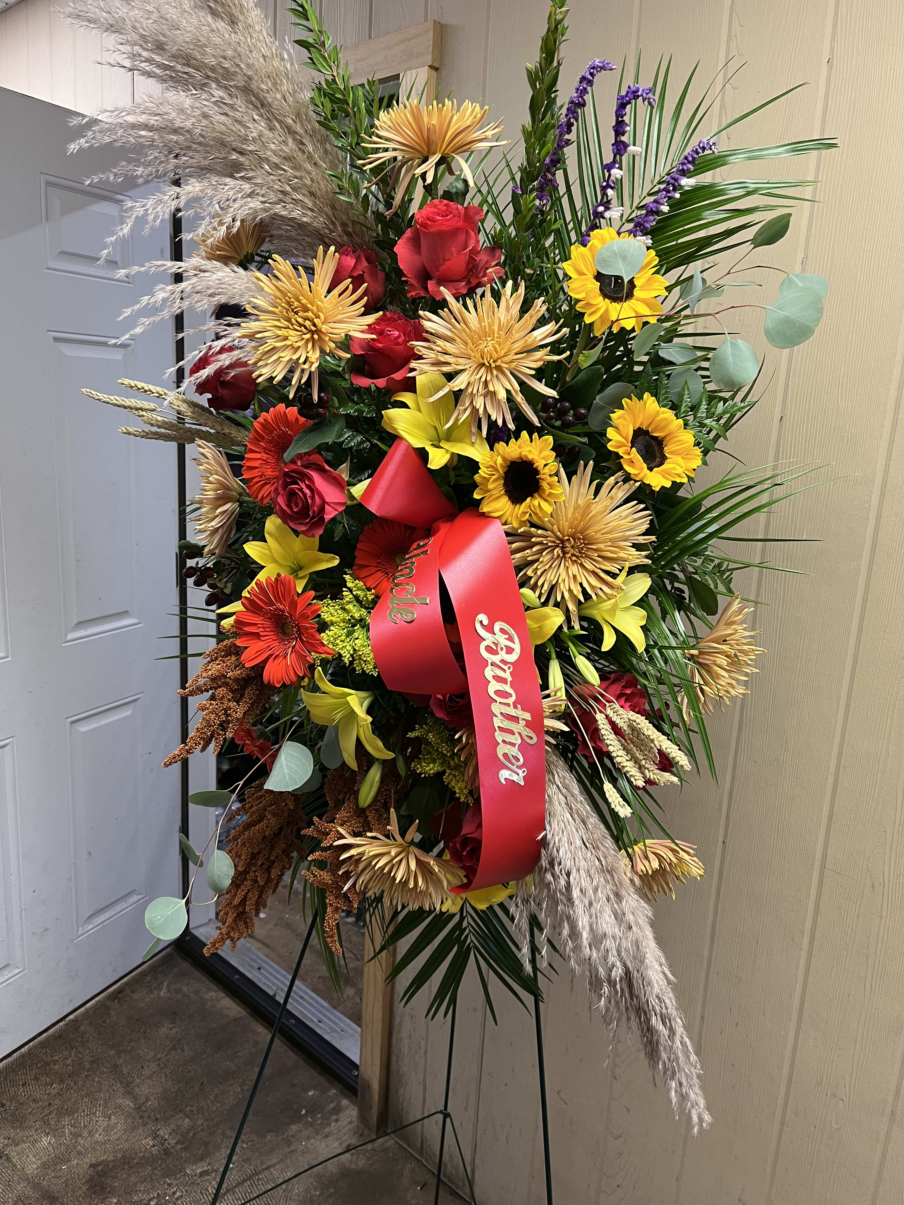 Tall standing floral spray with red and yellow flowers and a red ribbon