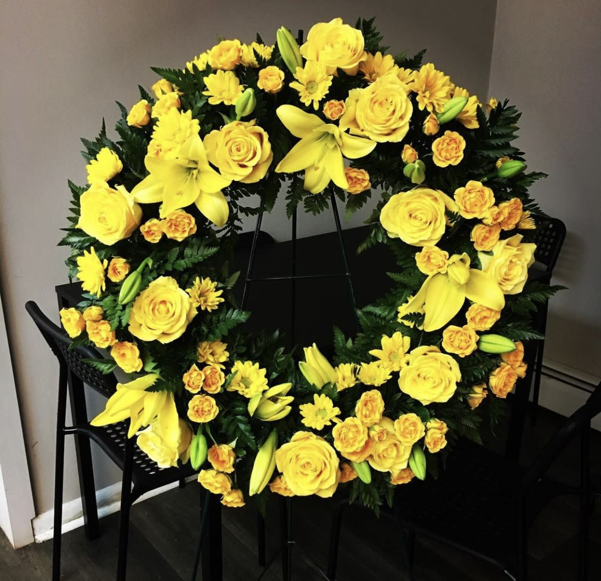 Yellow floral wreath with roses, lilies, and daisies on a stand