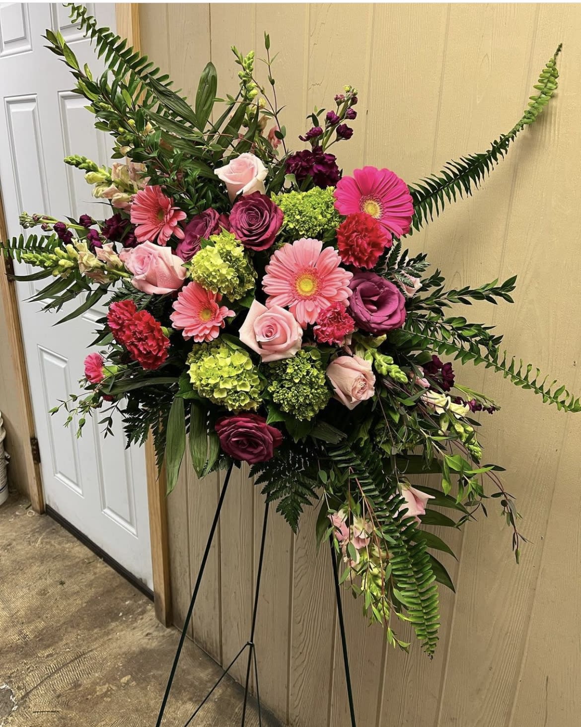 Standing floral spray with pink and burgundy blooms on a black easel