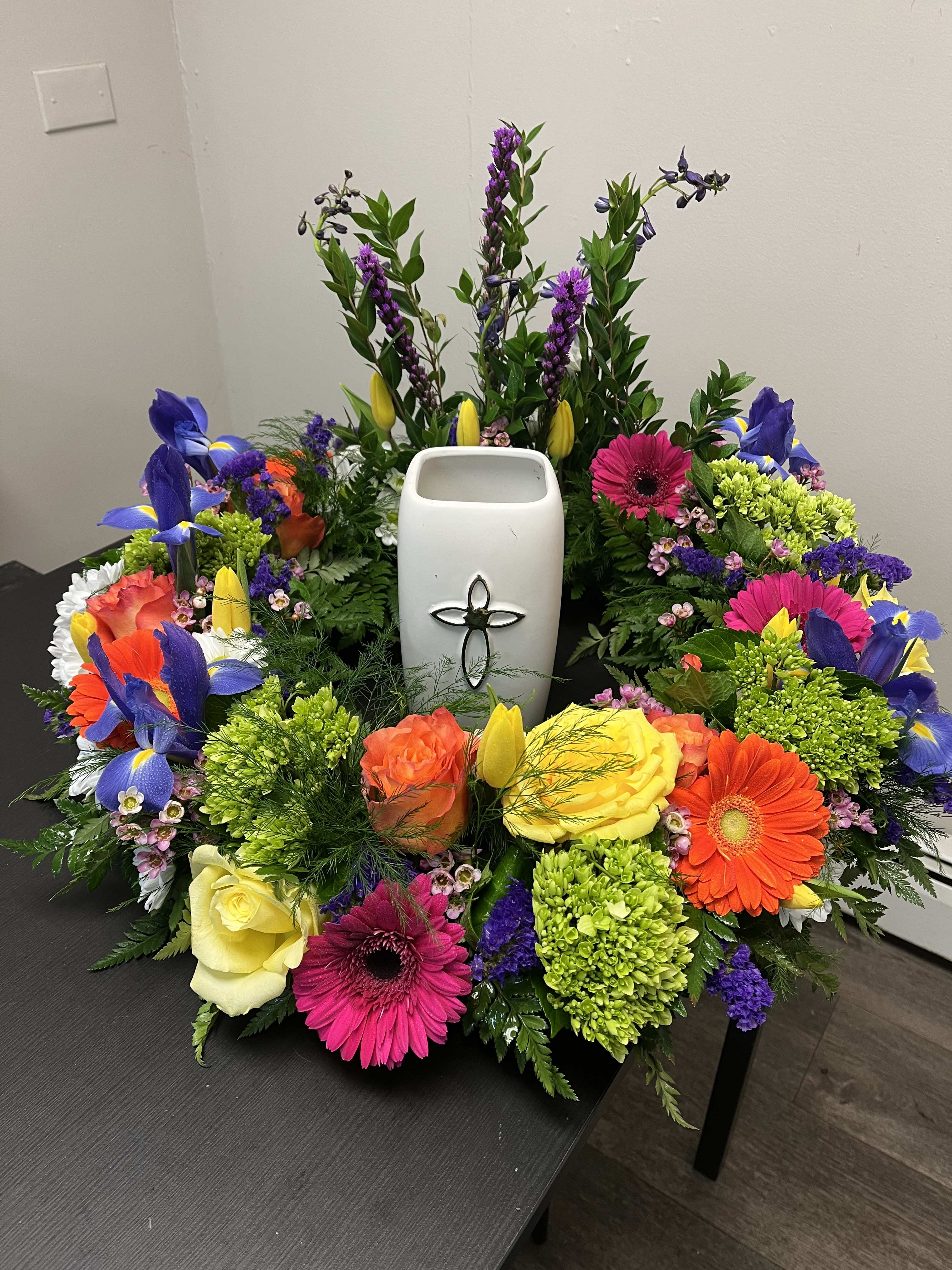 Colorful floral wreath around a white urn with a cross emblem