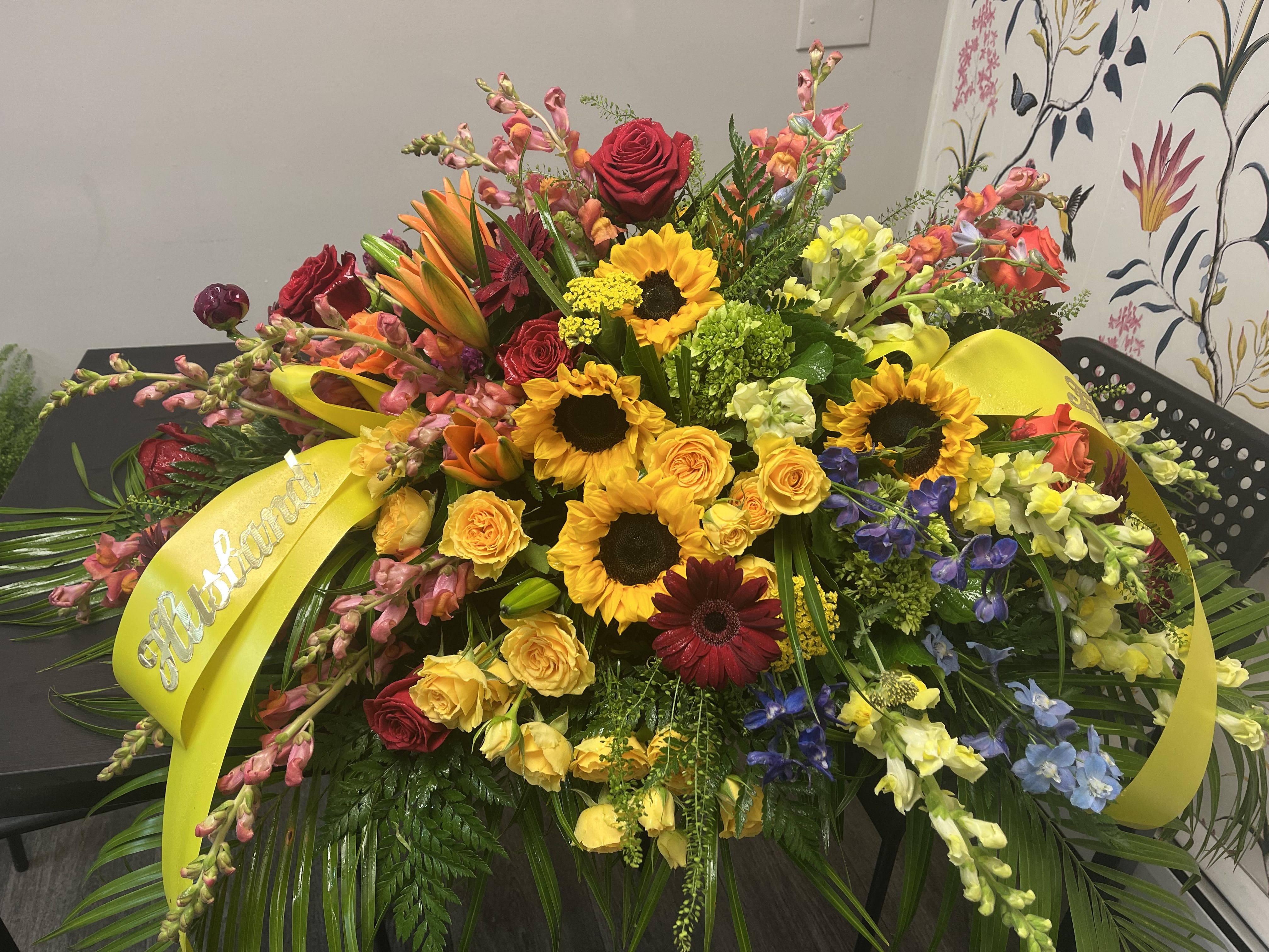 Large mixed flower spray with yellow ribbon and roses, sunflowers, and lilies