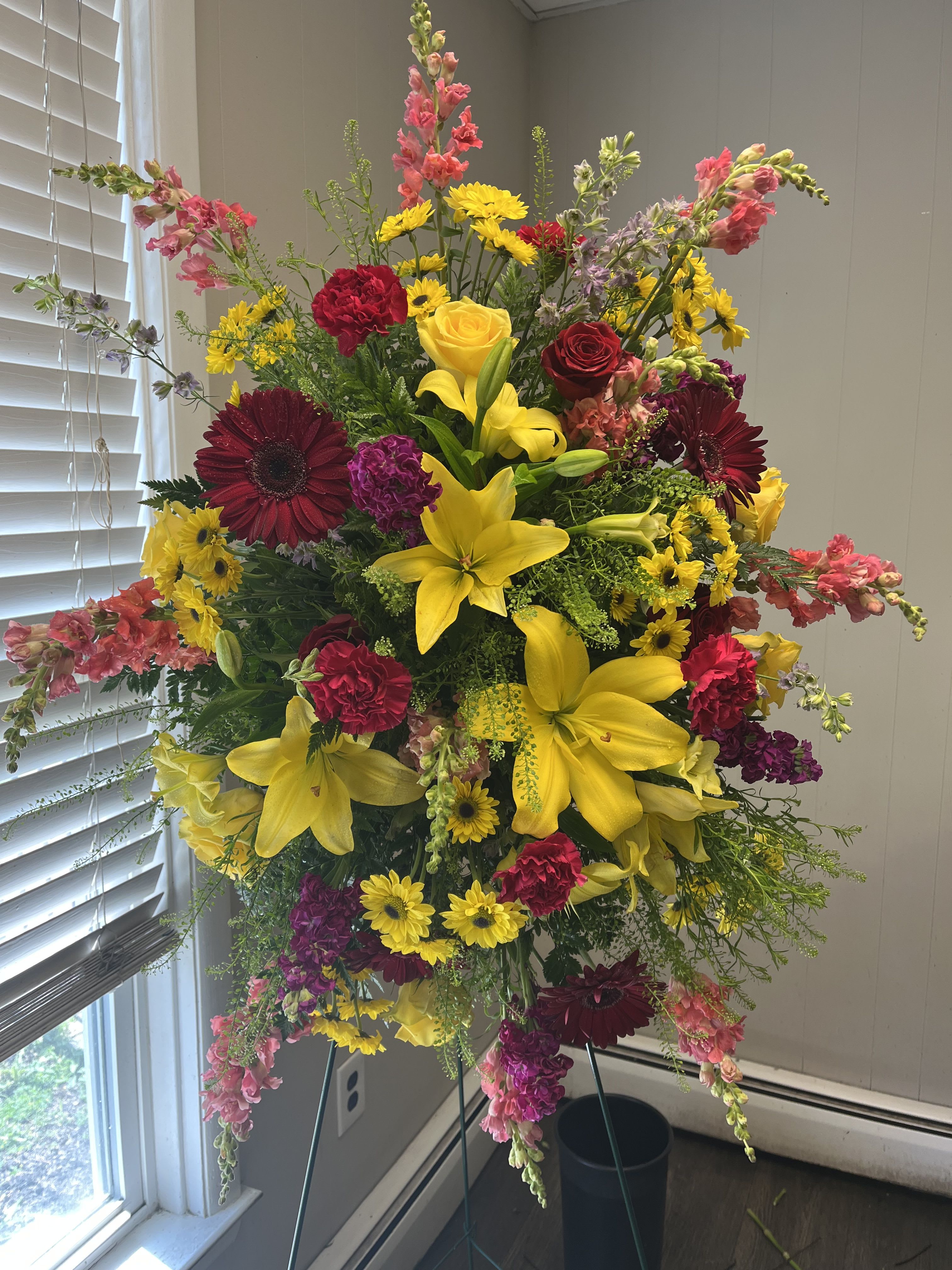 Primary color standing spray  - Designers choice of primary colored flowers, arranged in a standing spray. The perfect addition to any funeral service. Script can be added. Include in the special instructions what you would like the script to say. Examples such as mother, father, grandparent, sibling, aunt or uncle, etc.