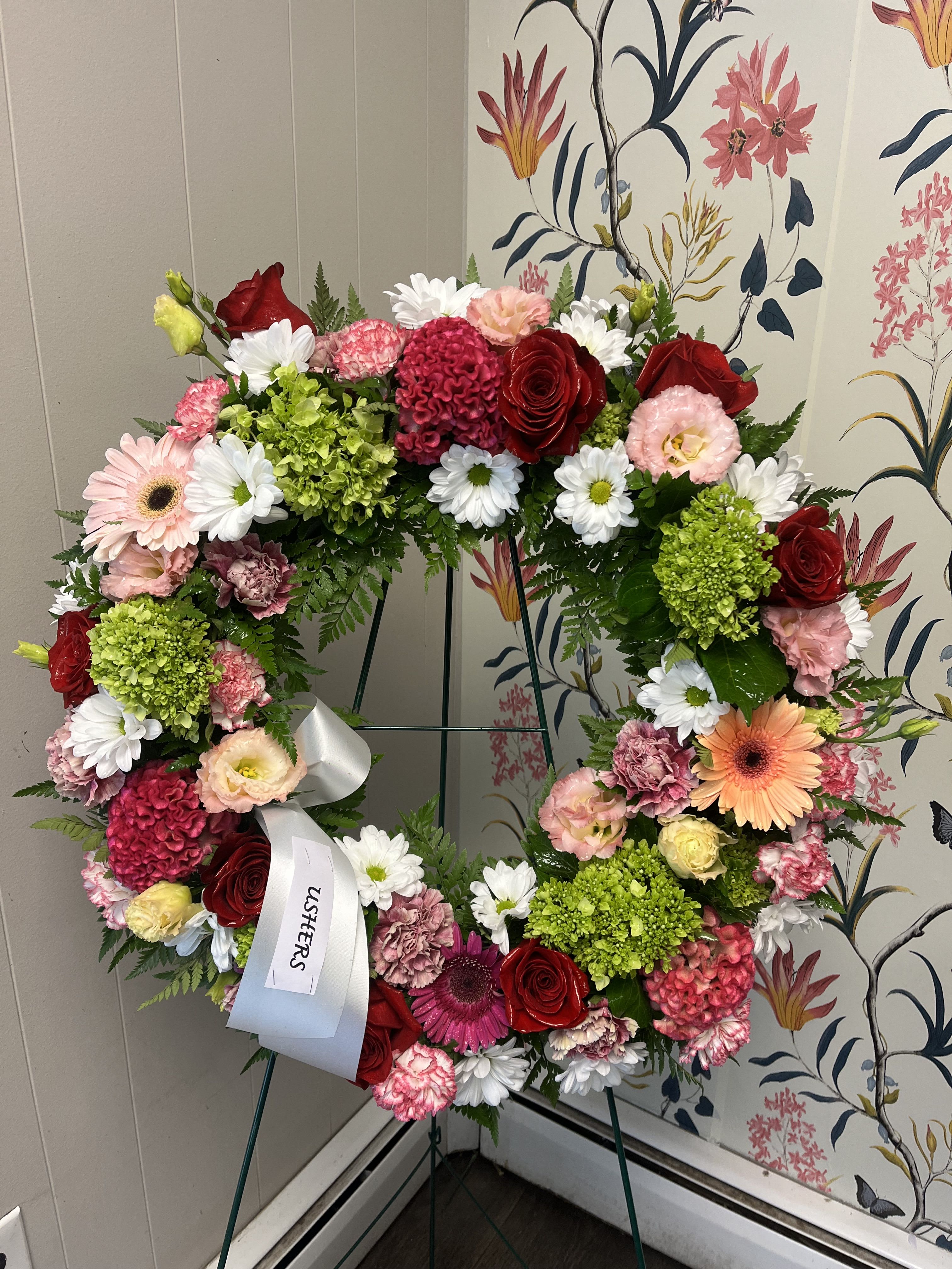 Heart-shaped floral wreath with roses, daisies, and carnations on an easel