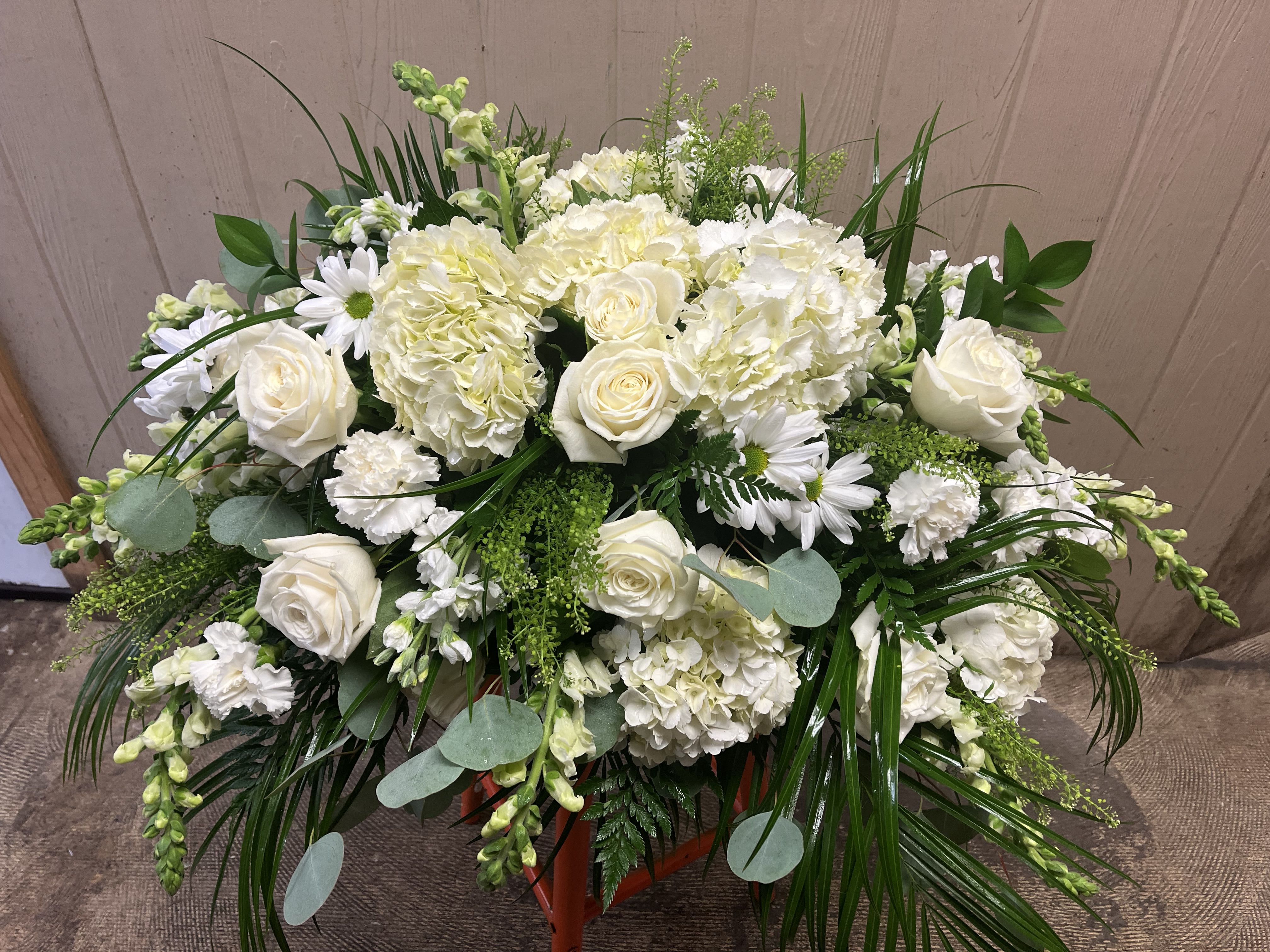 All white casket spray  - This half casket spray is filled with elegant white hydrangea, roses, snap dragons, stock, carnations and asst greens. 