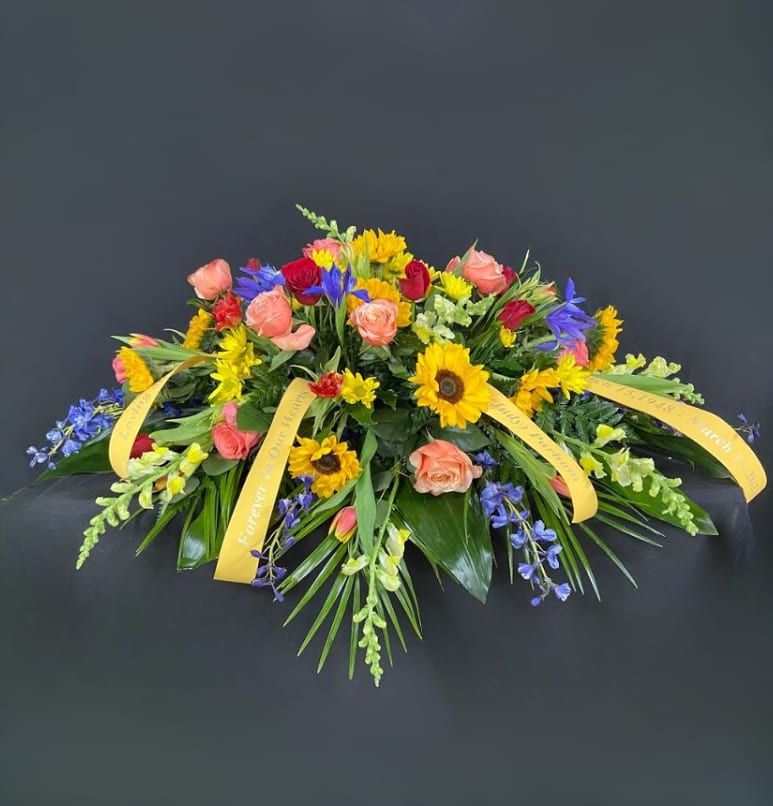 Colorful floral casket spray with roses, sunflowers, and blue accents