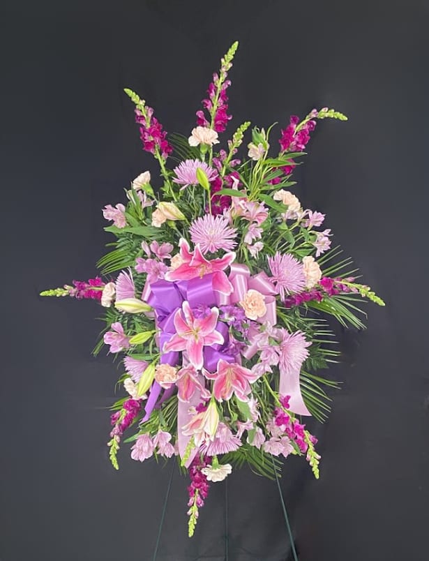 Pink and purple funeral spray with lilies and ribbon on an easel