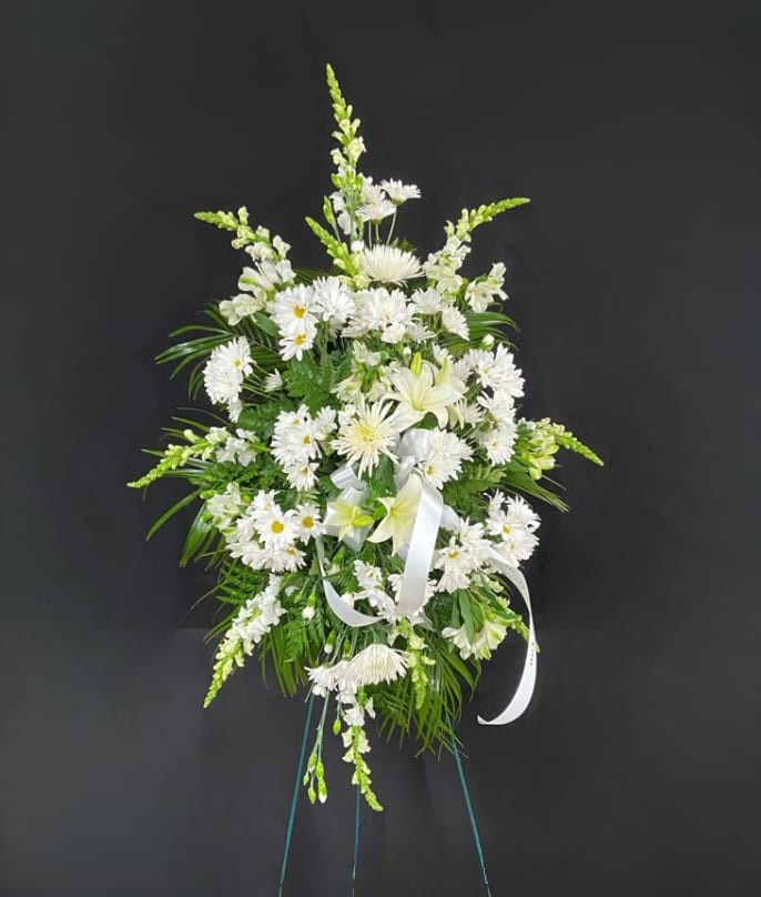 Tall standing spray of white flowers with a white ribbon on an easel stand