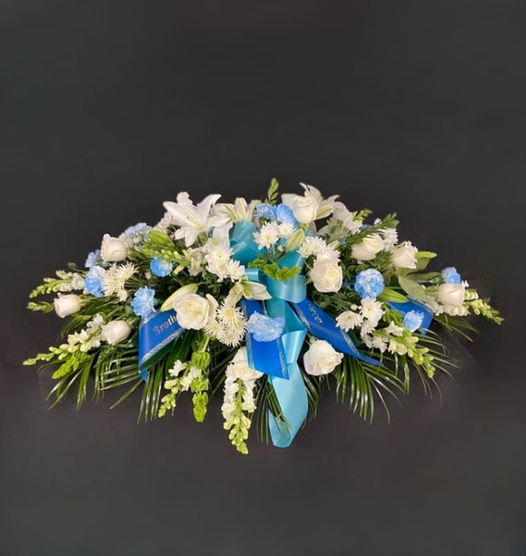 Light Blue and White Mixed Casket Spray - Blue carnations and/or mums are surrounded by a mix of white flowers such as roses, lilies, gerbera daisies, fuji mums, daisy poms, snapdragons, and veronica. Price includes up to 4 custom printed ribbons.