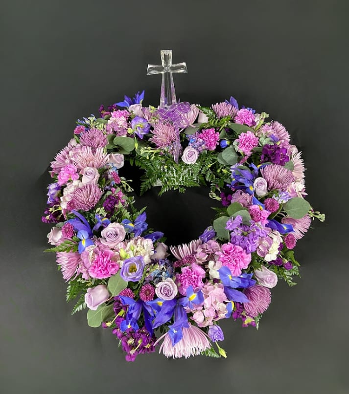 Circular wreath of purple and pink flowers with a clear cross topper