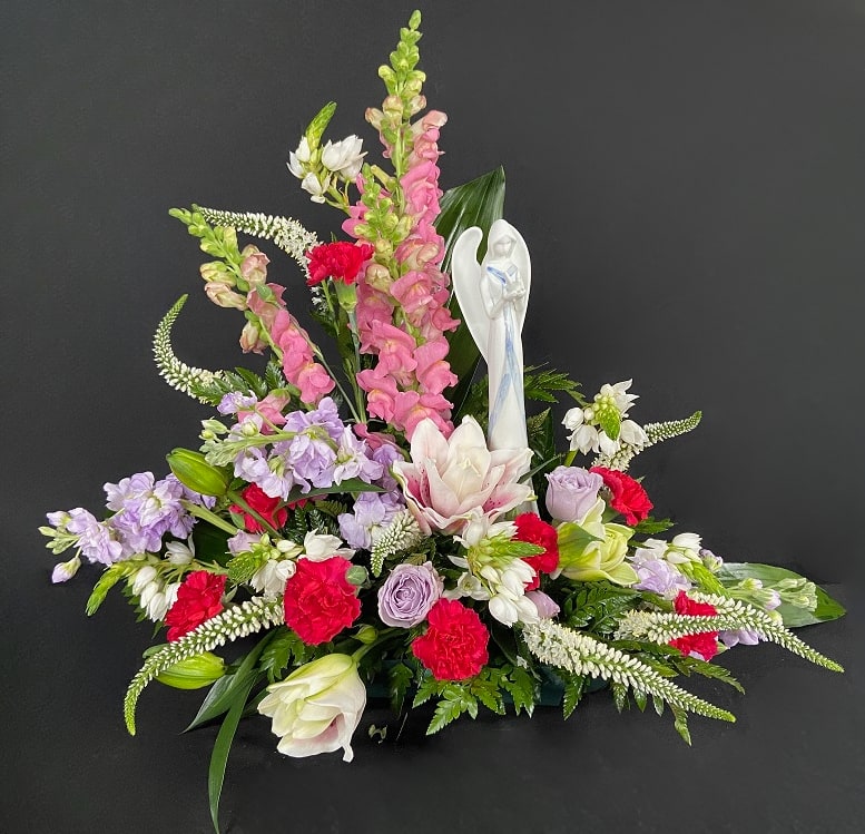 Sympathy floral arrangement with pink and white flowers and an angel figurine