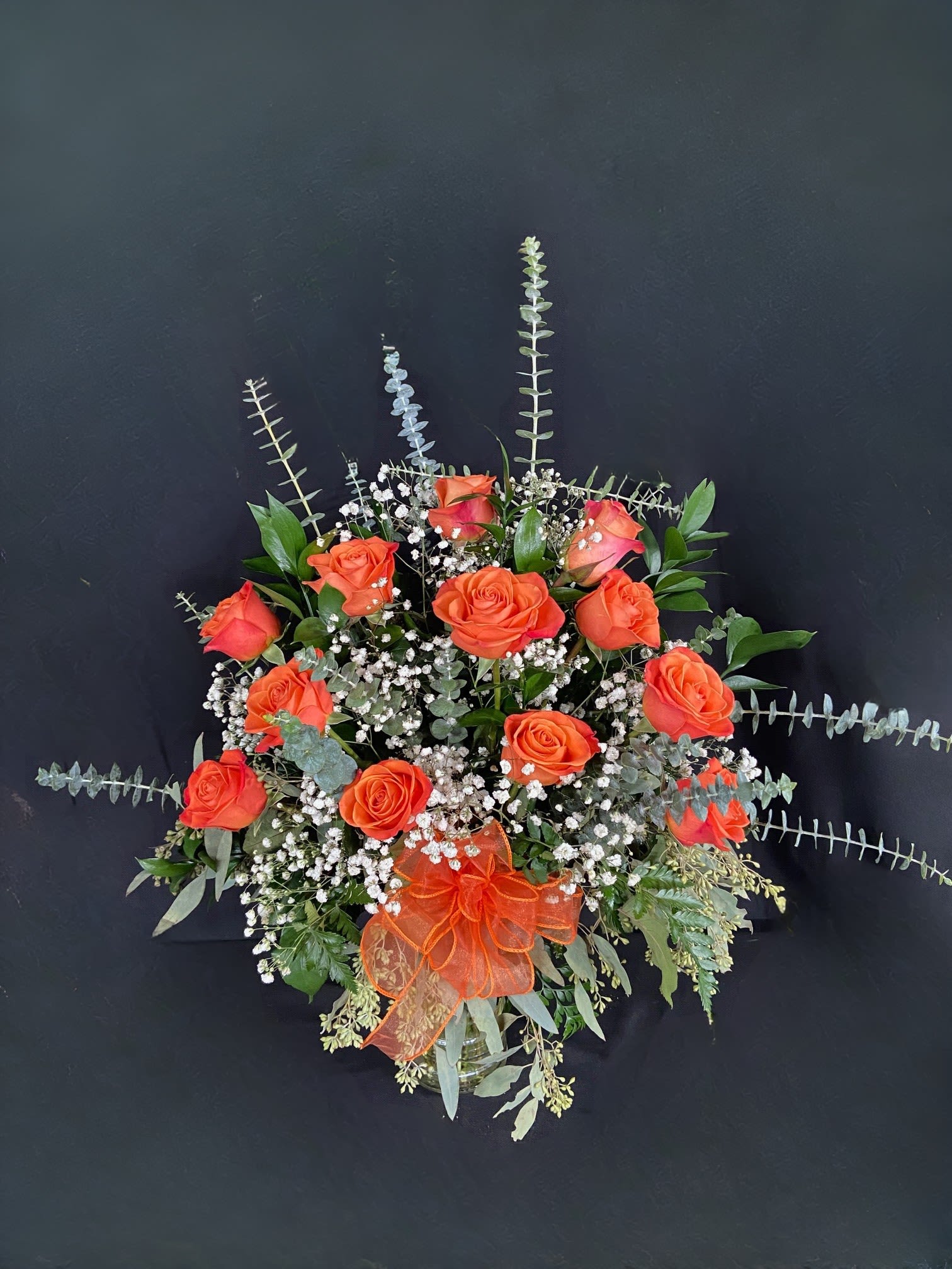 Orange roses in a glass vase with baby's breath and greenery