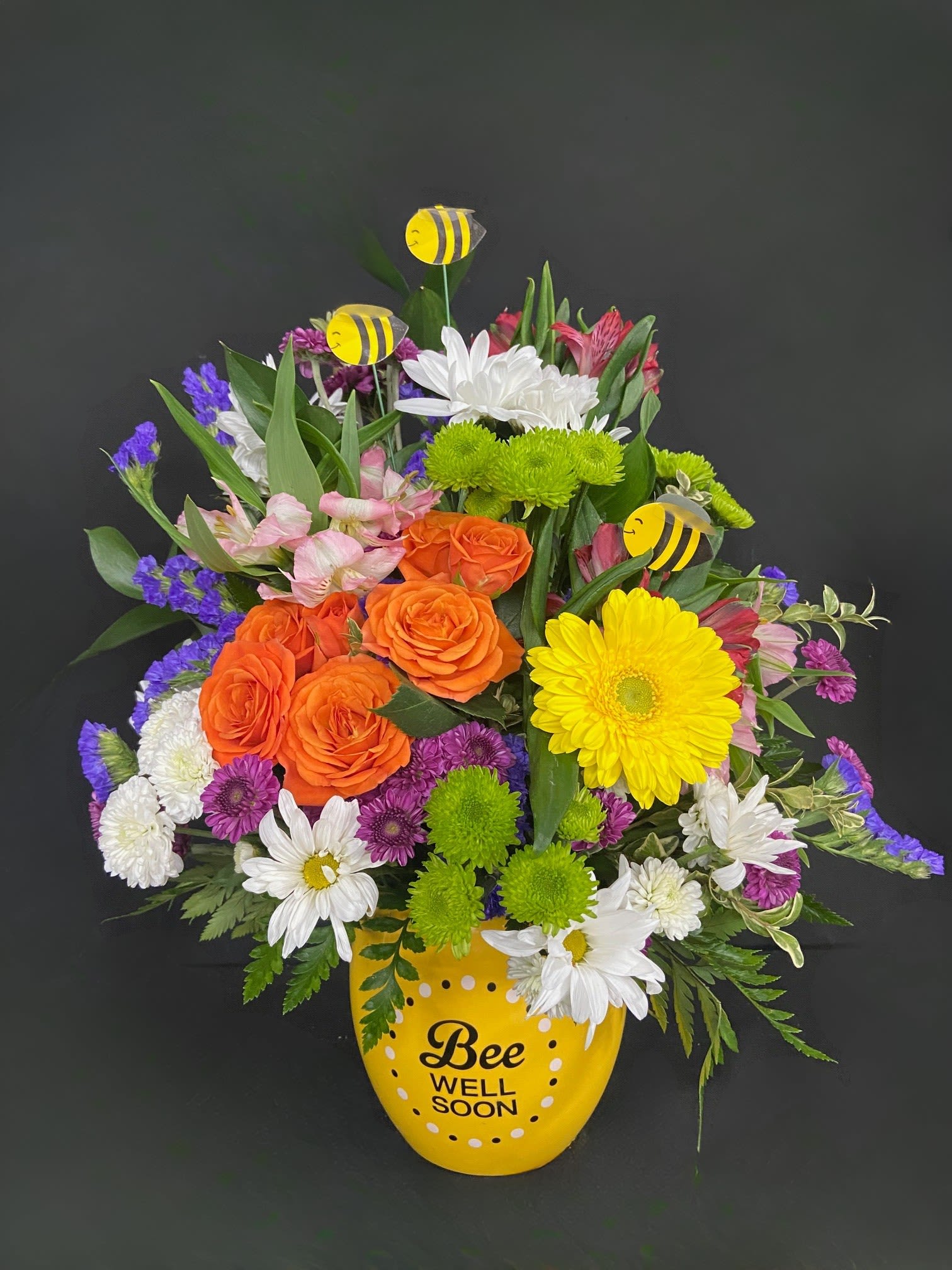 Buzzing Bee Well Pot of Flowers - Tiny bees float among a vibrant and beautiful garden of yellow Gerberas (or sunflowers if available), red alstro, peach roses, and white &amp; purple daisies.