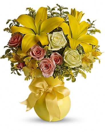 Yellow lilies and roses arranged in a gold vase with a ribbon bow