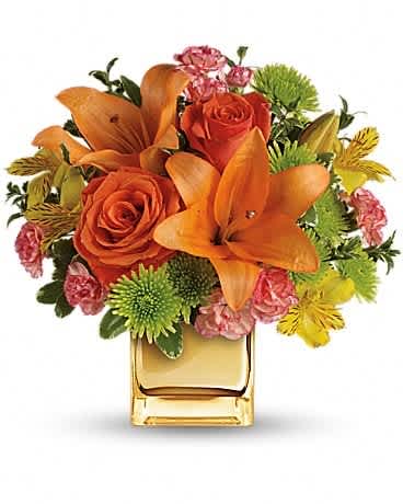 Orange roses and lilies in a square glass vase with pink and green accents