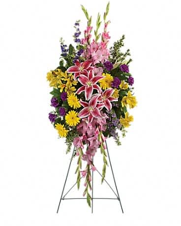 Standing floral spray with pink lilies, yellow daisies, and purple flowers on an easel