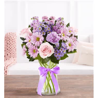 Pink and lavender bouquet in a clear glass vase with a purple ribbon