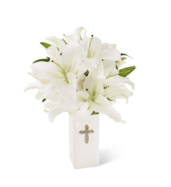 White lilies arranged in a tall white vase with a cross emblem
