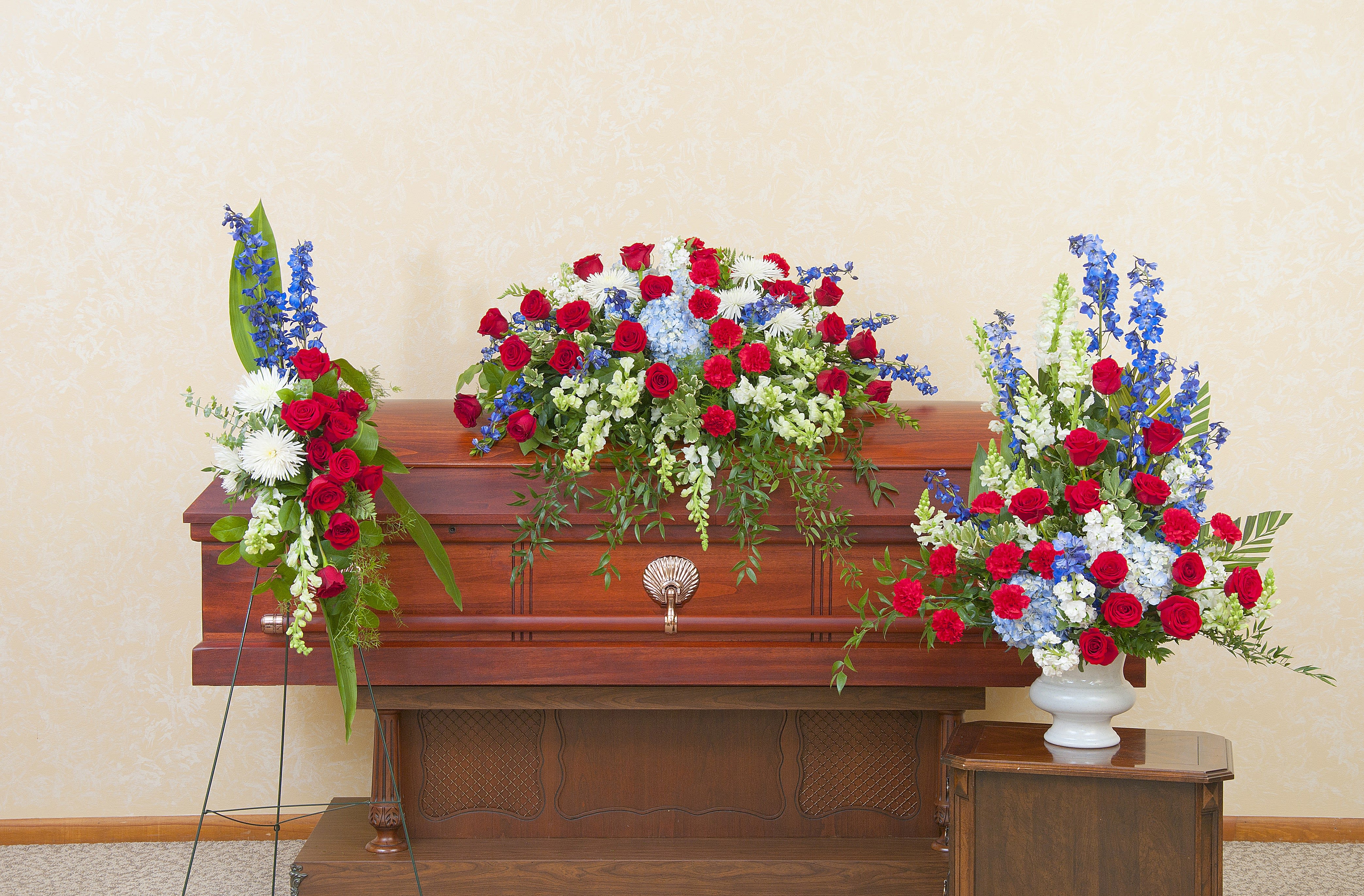 Casket spray with red, white, and blue flowers on a wooden casket