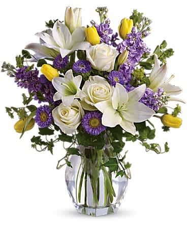 White lilies, roses, and purple flowers arranged in a clear glass vase