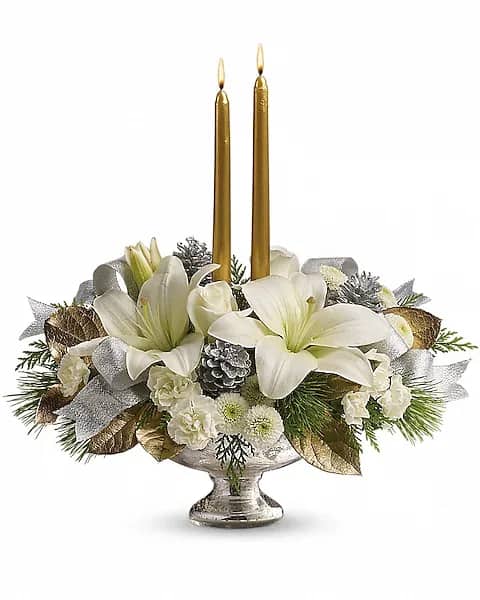 White floral centerpiece with two gold taper candles in a silver pedestal bowl