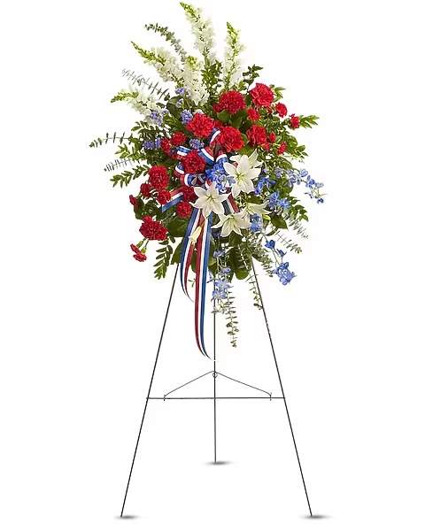 Standing floral spray with red carnations, white lilies, and blue accents on an easel