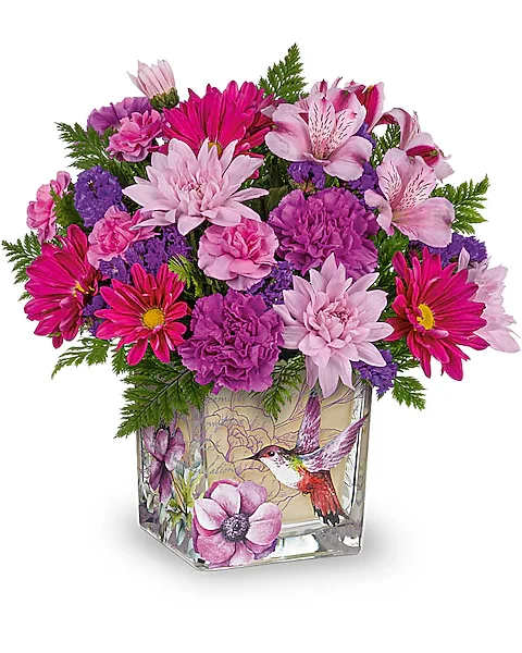 Teleflora's Love In Flight Bouquet - A flight of fancy on Mother's Day or any special occasion, this pretty purple bouquet looks especially enchanting thanks to a keepsake glass cube with vintage botanical motif. Purple carnations, lavender cushion spray chrysanthemums, lavender alstroemeria, purple daisy spray chrysanthemums and miniature lavender carnations are arranged with leatherleaf fern. Delivered in a Sweet Hummingbird cube.