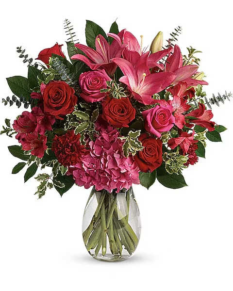 Bouquet of pink lilies, red roses, and hydrangea in a glass vase