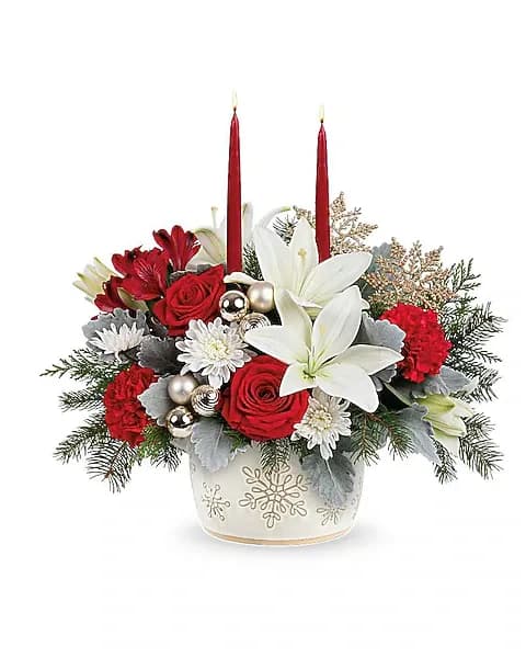 Holiday arrangement with red roses, white lilies, and two red candles in a snowflake vase