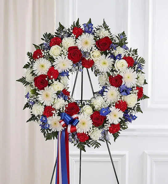 Red, white, and blue floral wreath on a black stand with ribbon