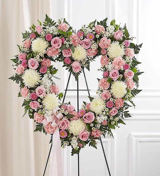 Heart-shaped standing wreath of pink roses, pink carnations, and white mums with a pink ribbon bow