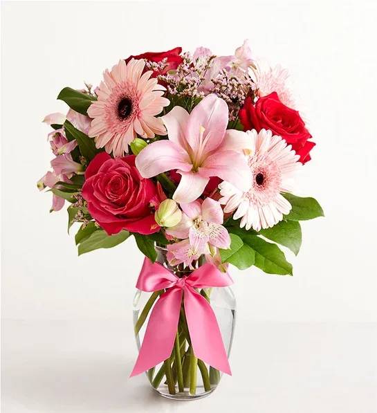 Pink and red mixed bouquet in a clear glass vase with a pink ribbon