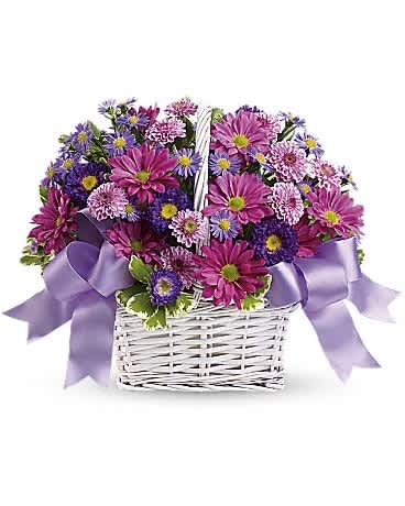 Purple and pink mixed flowers in a white wicker basket with lavender ribbon