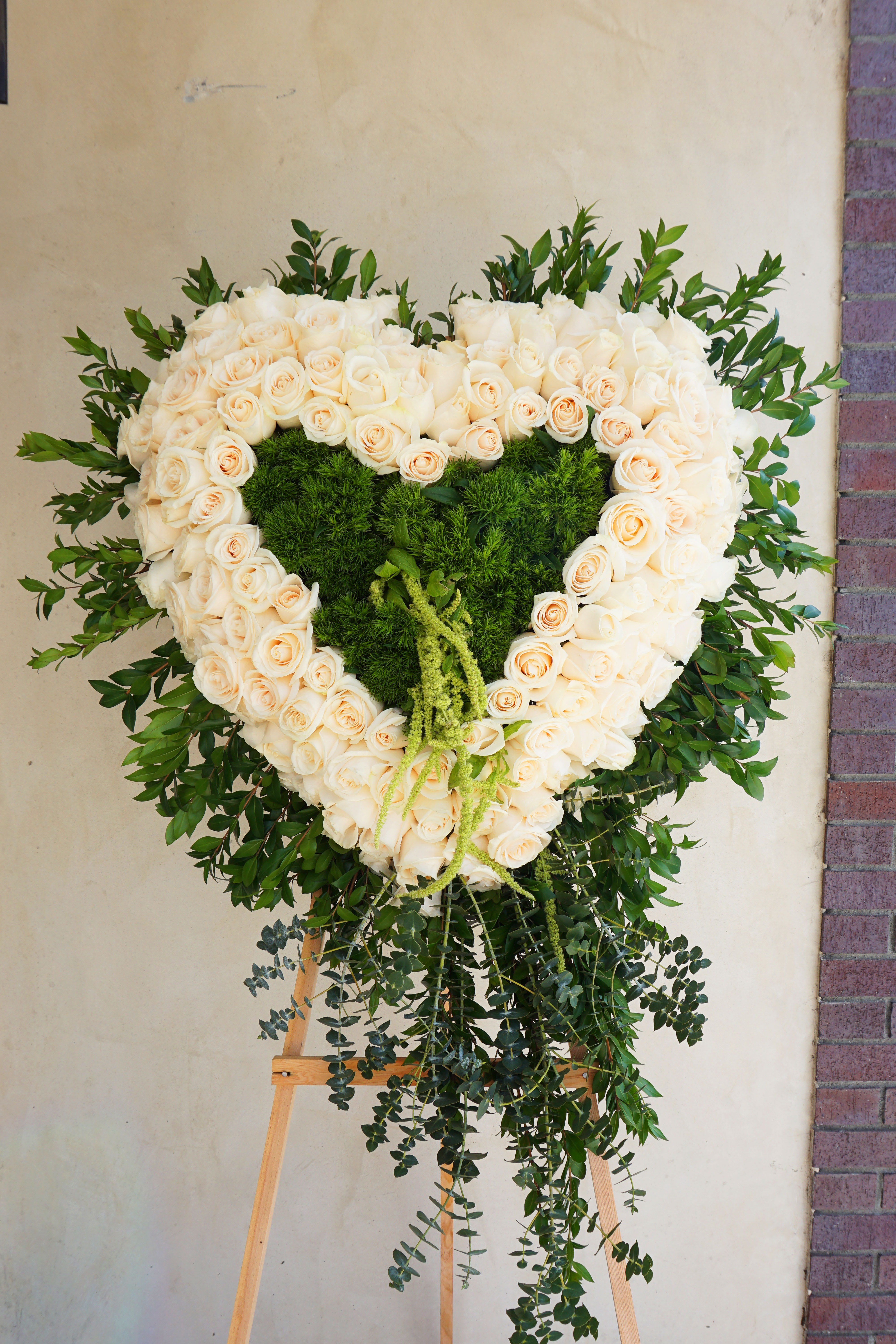 Heart-shaped white rose wreath on an easel with green foliage