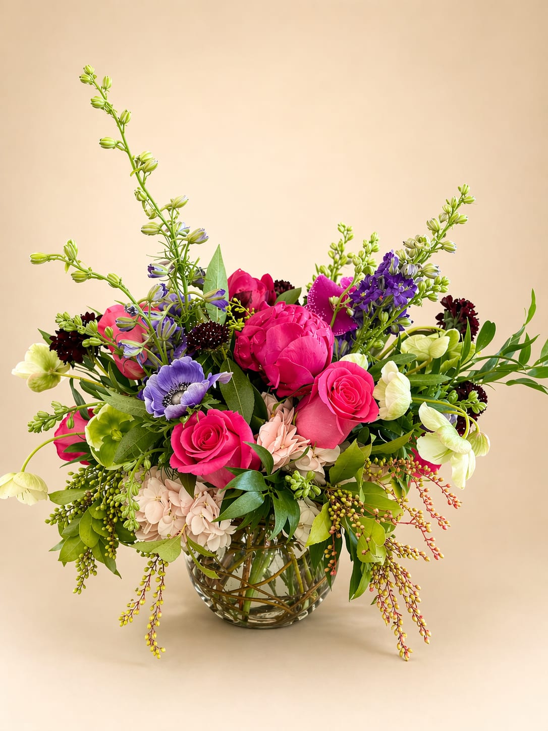 Dragonfruit Infusion - Vibrant, playful, and effortlessly chic, the Dragon Fruit Infusion arrangement dazzles with a palette of hot pinks, blush, and rich purples. Designed in a small fishbowl vase artfully lined with curly willow. Light pink hydrangeas create a soft, cloud-like base, while Pink Floyd roses &amp; peonies add a bold pop of fuchsia. Striking purple anemones, phalaenopsis orchids, and delicate purple larkspur bring moody elegance, complemented by airy scabiosas and hellebores.  Seasonal greenery adding fresh movement and balance.  Perfect for adding a splash of modern sophistication to any space, this arrangement is as bold and refreshing as its namesake fruit—a true statement piece bursting with color and style.