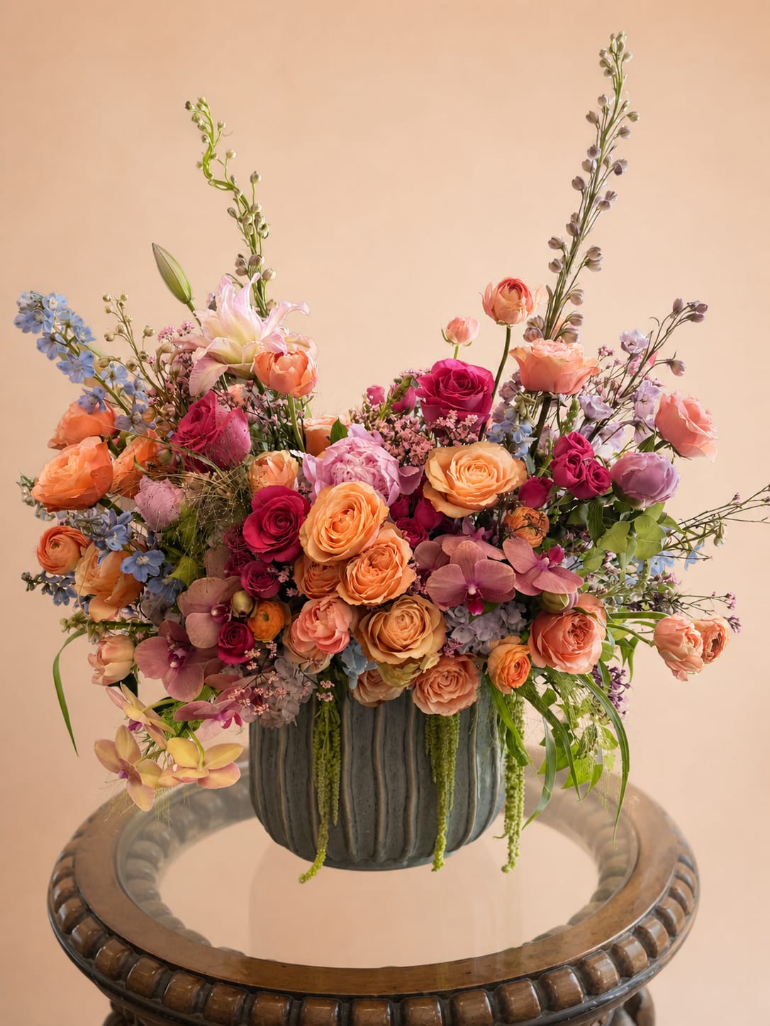 Wildflower Wishes - A whimsical breath of fresh air, "Wildflower Wishes" captures the magic of a spring morning in full bloom. This lush, garden-style design features a vibrant mix of sun-kissed roses &amp; exotic orchids, accented by airy wildflowers that dance above a textured, stone-blue vessel. It's a perfectly untamed tribute to the beauty of a new day.