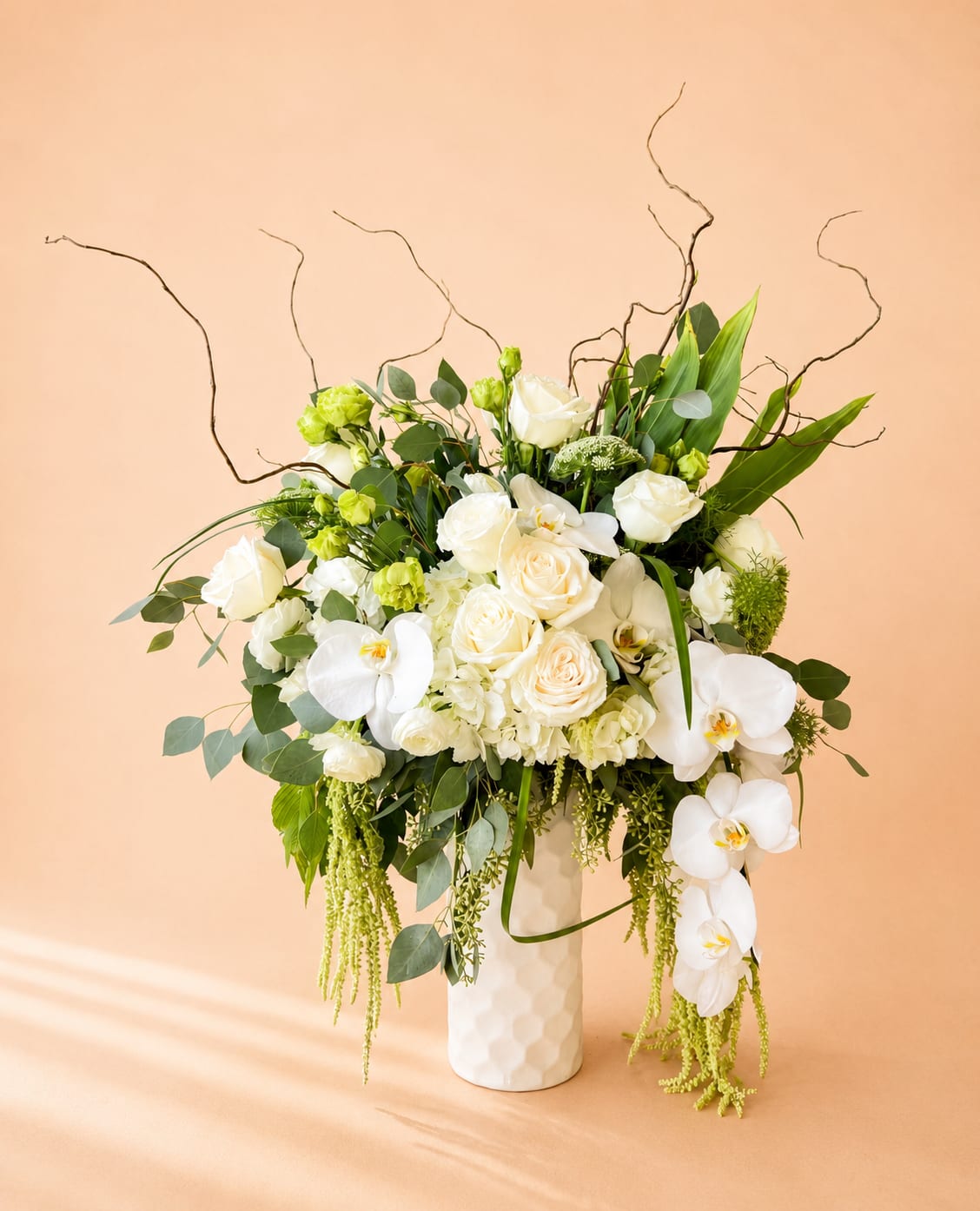 White roses and orchids in a tall white vase with greenery